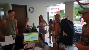 Um grupo de pessoas em uma sala com um computador exibindo uma página da web, um relógio na parede e uma porta com uma placa.