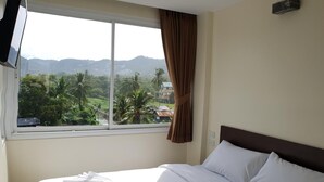A hotel room with a bed, a window with a view of mountains and greenery, and a curtain. - Top Hostel Samui (Koh Samui)