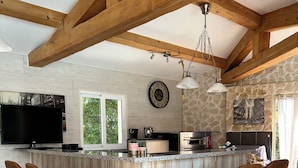 Una cocina con isla de madera, taburetes de bar, televisor de pantalla plana y paredes de piedra.