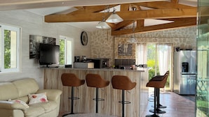 Una cocina moderna con protector mural de piedra, vigas de madera y una zona de bar con taburetes.