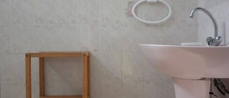 A bathroom with a white sink, a wooden shelf, and a glass shower enclosure.