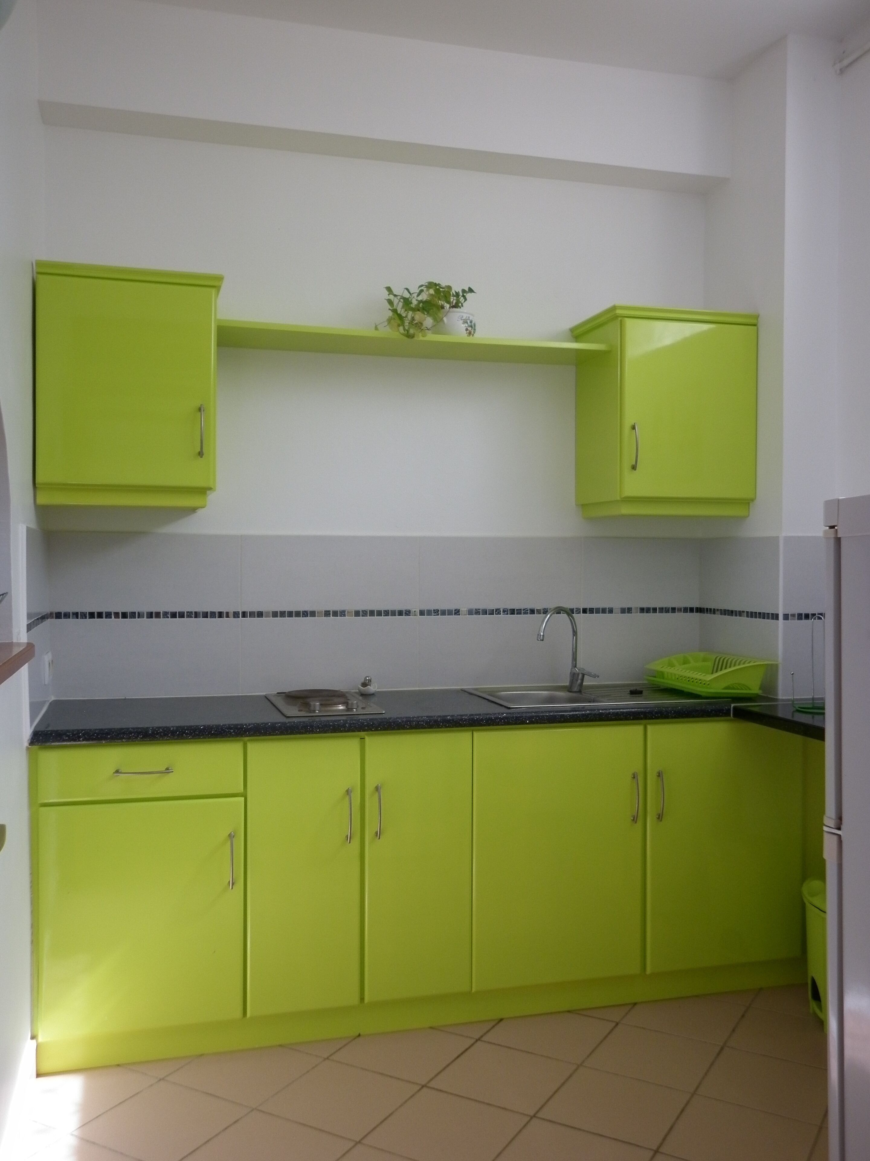Una cocina con armarios verdes, encimera negra y salpicadero de azulejos.