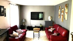 A living room with two red leather sofas, a flat-screen TV, a coffee table, and artwork on the walls. - House with independent studio and pool in a village in the heart of the Alpilles (Paradou)