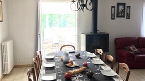 A dining area with a round table set for six, surrounded by wooden chairs. A black tablecloth with a white floral pattern covers the table. There is a chandelier hanging above the table, and a red sofa is visible in the background. - House with independent studio and pool in a village in the heart of the Alpilles (Paradou)