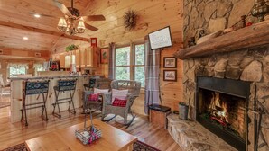 L’intérieur chaleureux d’un chalet avec une cheminée en pierre, un plafond en bois et un coin bar équipé de tabourets.