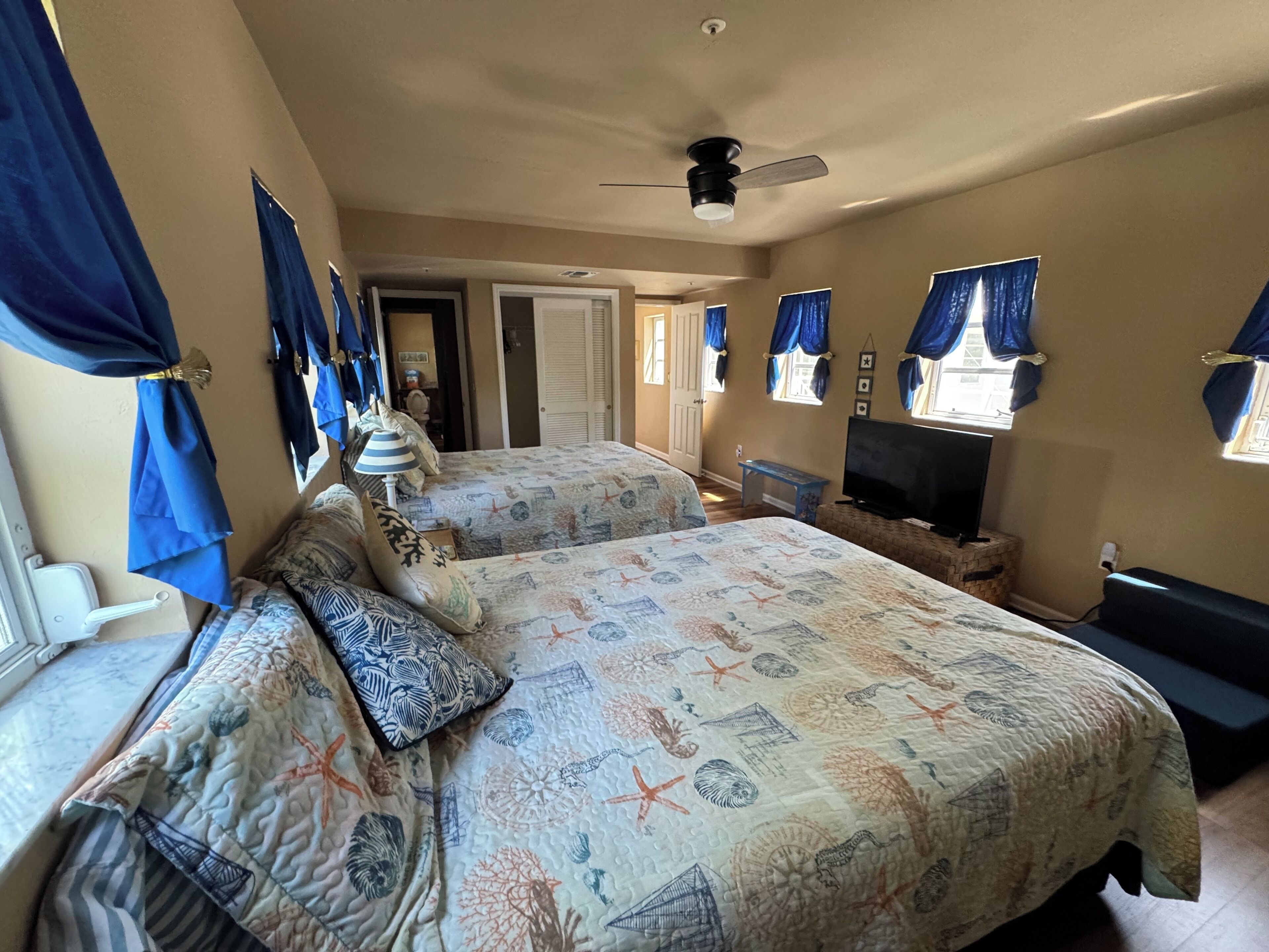 A bedroom with two beds, a ceiling fan, a TV, and a window with curtains.