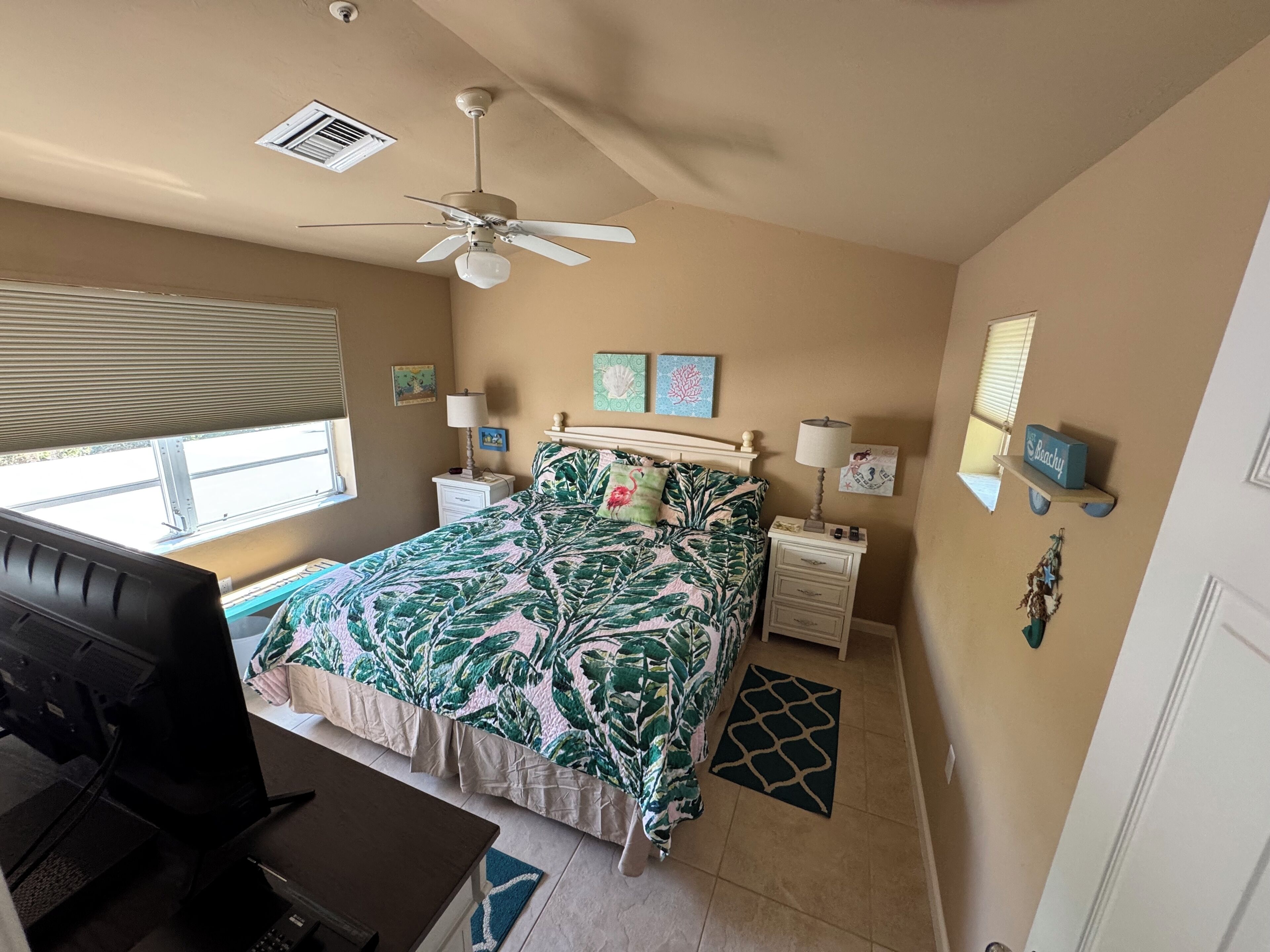 A bedroom with a bed, a desk, a ceiling fan, and a window.
