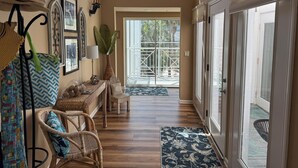 A hallway with a wooden floor, wicker furniture, a patterned rug, and a view of the outdoors through a glass door.