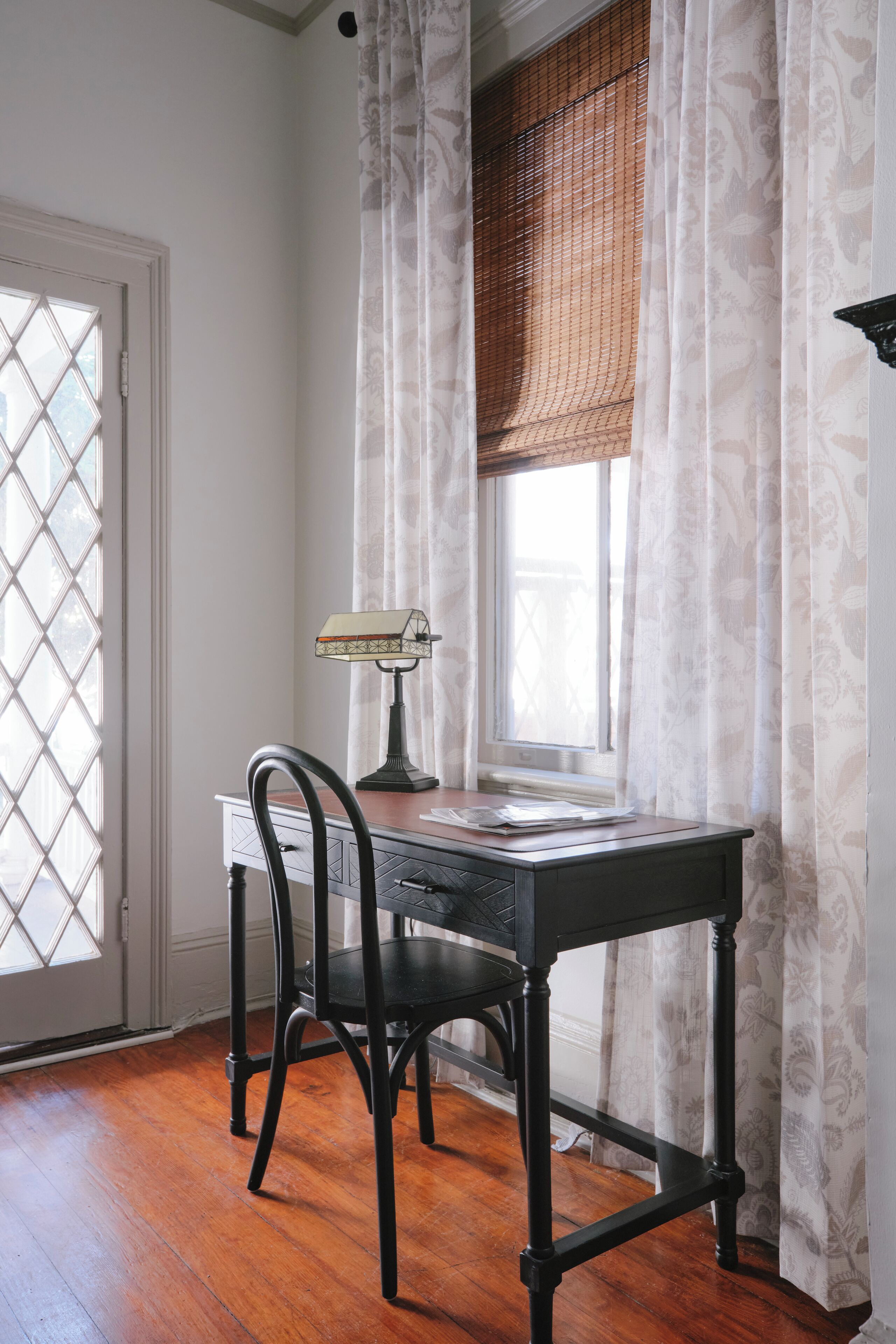 A room with a wooden desk, a chair, a lamp, and a window with curtains.