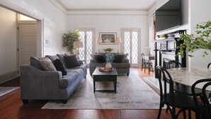 A living room with two sofas, a coffee table, and a dining table with chairs. There is a TV mounted on the wall and a fireplace. - Comfortable Escape 2BR Historic Downtown (Savannah)