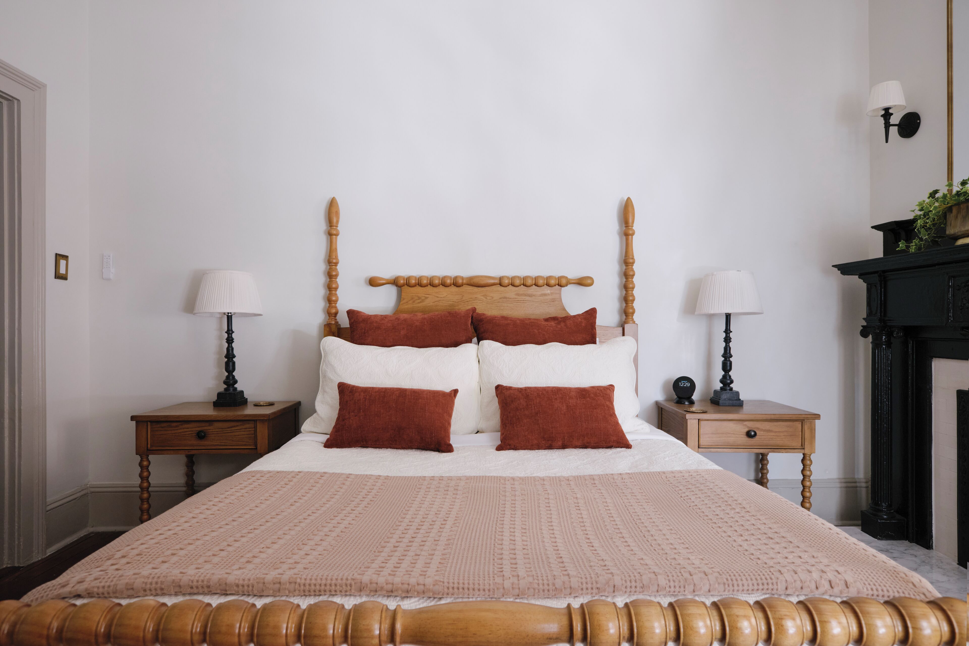Uma cama bem arrumada com cabeceira de madeira, duas mesas de cabeceira com abajures e uma lareira.