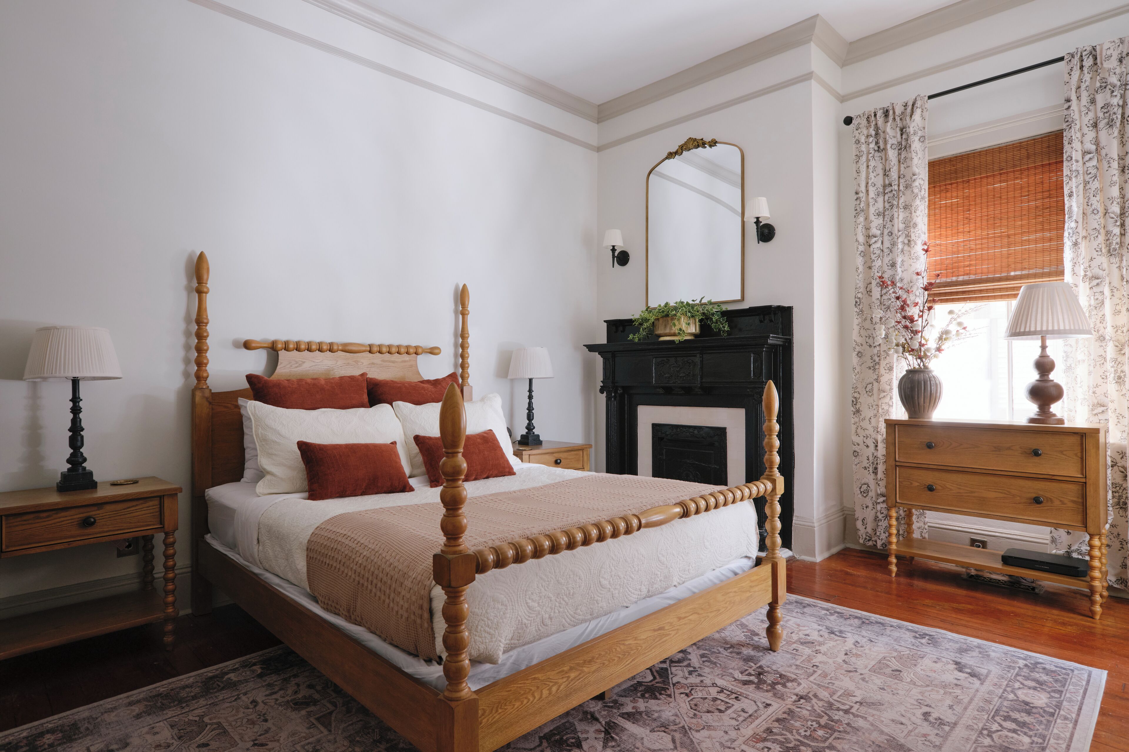 A neatly arranged bedroom with a wooden four-poster bed, a fireplace, and a nightstand with a lamp.