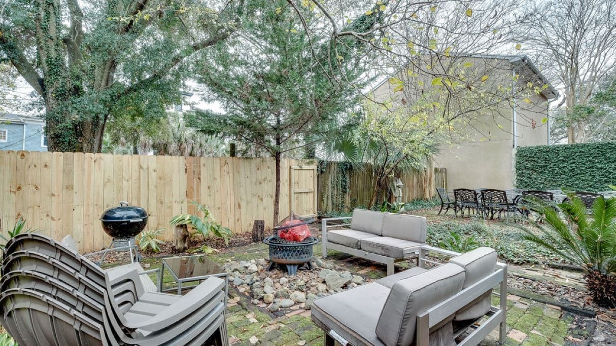 A backyard with a wooden fence, outdoor furniture, a fire pit, and various plants.