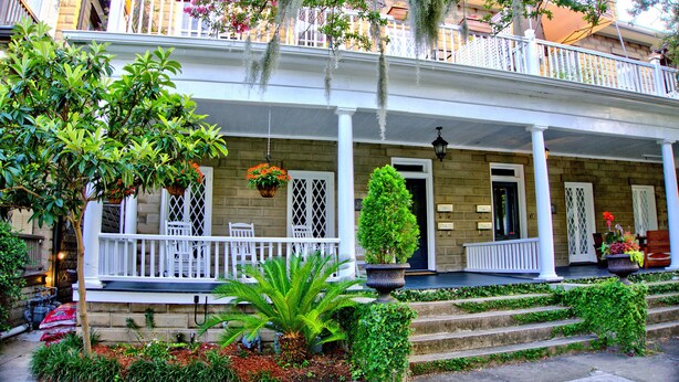 A two-story building with a covered porch, steps leading up to the entrance, and potted plants. - Comfortable Escape 2BR Historic Downtown (Savannah)