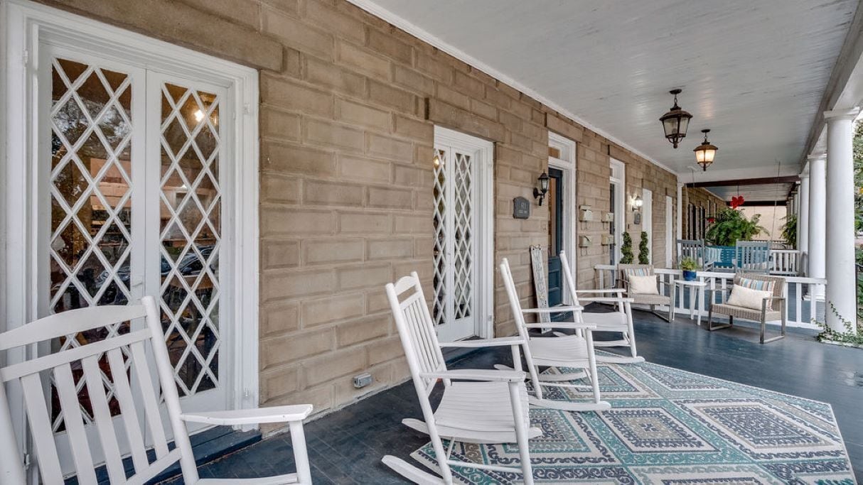 A covered porch with white wicker chairs and a patterned rug.