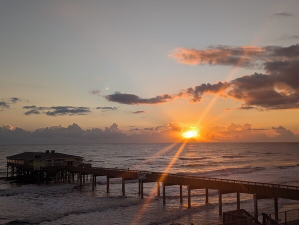 A pier extending into the sea with a building at the end, under a sunset sky.