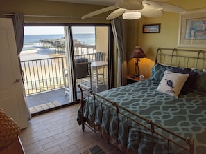 Una stanza con un letto, un comodino, una lampada, una sedia e vista sulla spiaggia e sul molo attraverso una porta scorrevole in vetro.