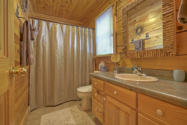 A wooden cabin bathroom with a shower curtain, toilet, wooden cabinets, and a sink with a mirror above it.