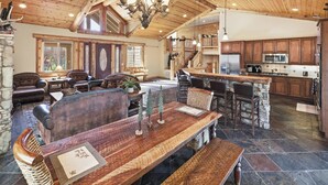Amplia sala de estar con techo de madera, chimenea de piedra y una gran mesa de comedor con bancos.