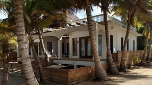 Una casa de playa con un porche cubierto, palmeras y arena.