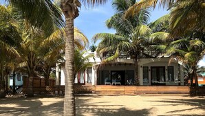 Propiedad frente a la playa con un espacio de estar al aire libre techado, palmeras y una playa de arena.