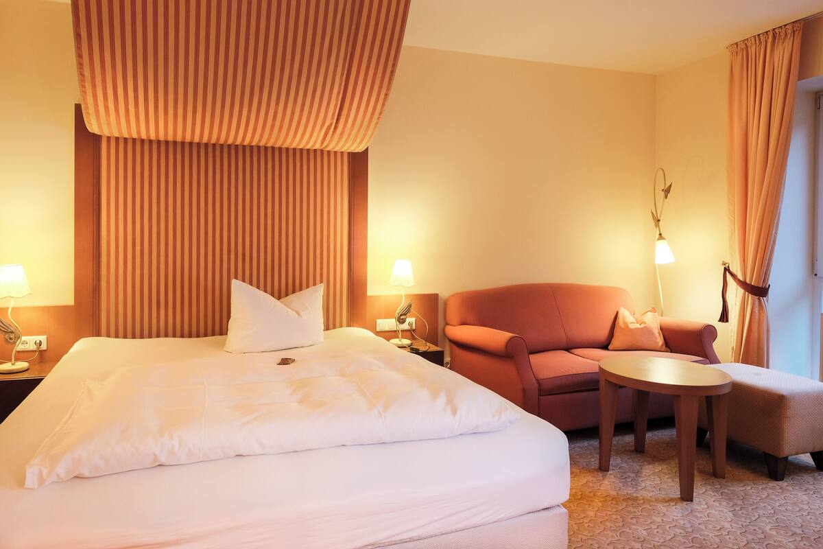 A hotel room with a large bed, a sofa, a small table, and two lamps.
