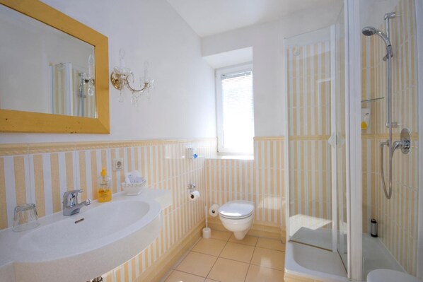 A bathroom with a large mirror, two sinks, a toilet, and a glass-enclosed shower area. - Burgblick (Hochburg-Ach)