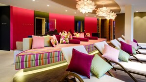 Um spa moderno com um sofá listrado e colorido, várias poltronas de descanso com almofadas coloridas e um lustre grande.