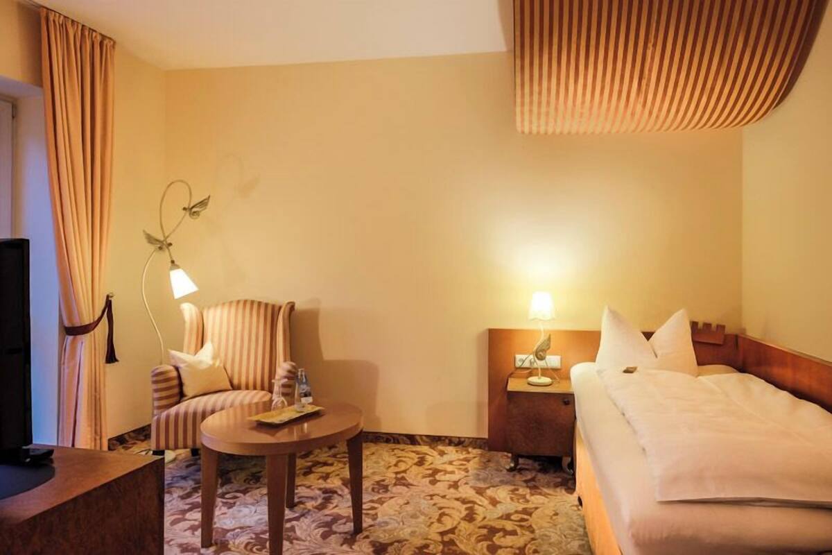 A hotel room with a bed, a sofa, a small table, a nightstand, and a television.