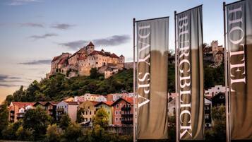 A historic castle on a hill with a river in the foreground and banners for a hotel.
