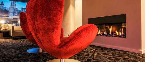 A modern living room with a red velvet armchair, a fireplace, and a view of a historic building through a large window.