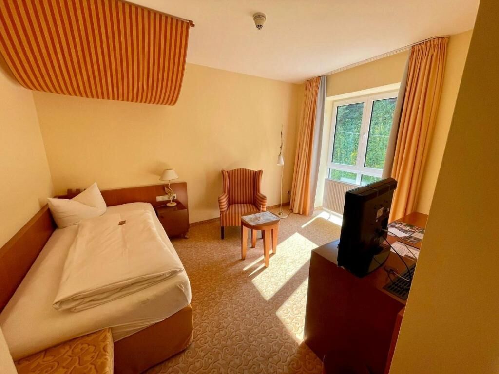 Een hotelkamer met een bed, een bureau met een televisie, een stoel en een raam met gordijnen.