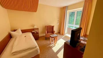 A hotel room with a bed, a desk with a television, a chair, and a window with curtains.