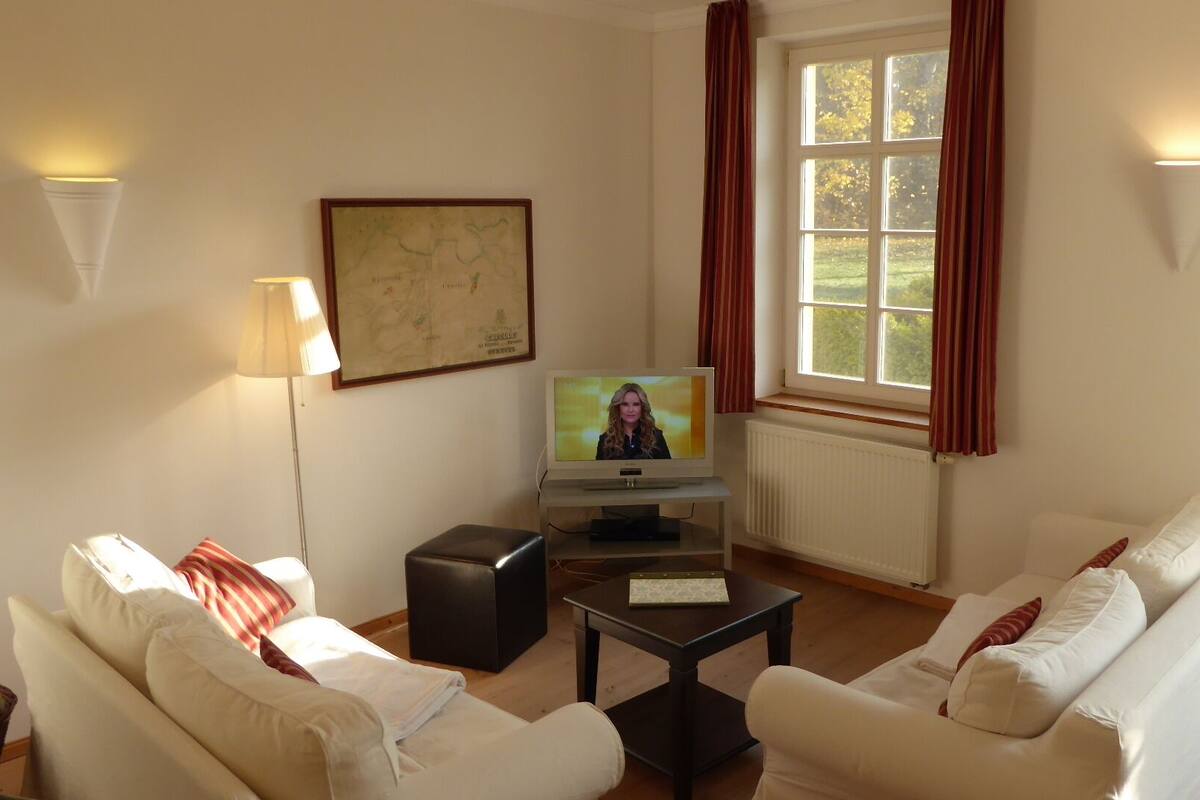 A living room with two white sofas, a television, a map on the wall, and a window with curtains.