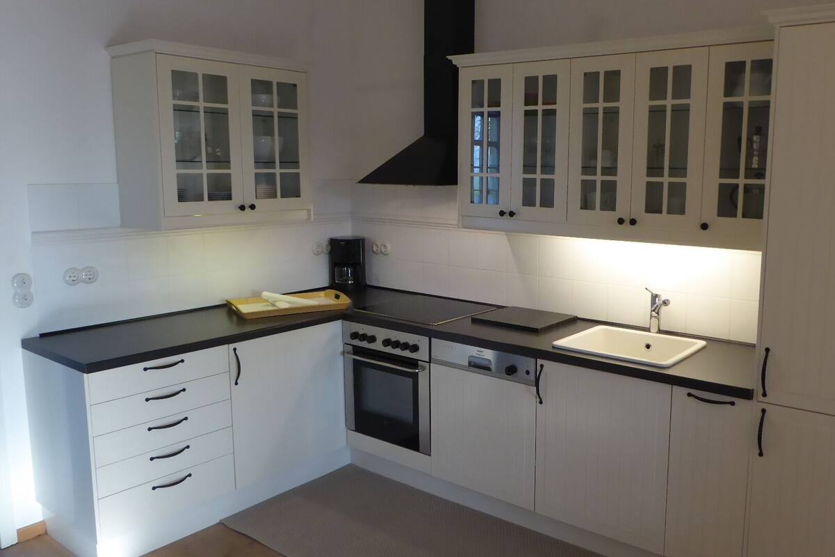 A modern kitchen with white cabinetry, a black countertop, a built-in oven, and a sink.