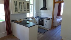 A compact kitchen with white cabinets, a black range hood, and a small island with a sink and a bowl. - Gut Rattelvitz (Gingst)