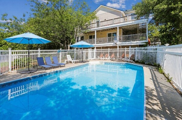 A swimming pool with lounge chairs and umbrellas, surrounded by a white fence, with a two-story building in the background. - HotTub, Pool Table, Elevator! Large fenced yard, pets (Duck)