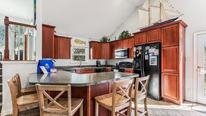 A kitchen with wooden cabinets, a black refrigerator, and a large island with bar stools.