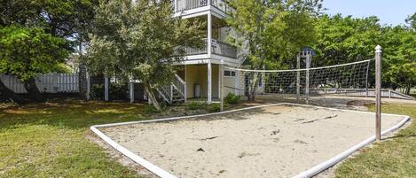 Una casa de dos pisos con balcón, cancha de voleibol y área cercada.