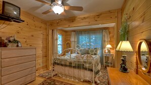 A wooden cabin bedroom with a bed, dresser, ceiling fan, and a television. - Toccoa River Escape | River Front | Gas Grill (Mineral Bluff)