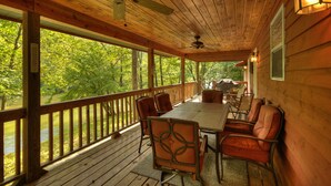 A wooden deck with a table and chairs, a ceiling fan, and a view of a river and trees. - Toccoa River Escape | River Front | Gas Grill (Mineral Bluff)