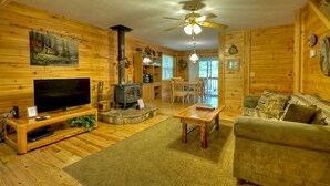 A cozy cabin interior with a wooden interior, a fireplace, a television, and a dining area. - Toccoa River Escape | River Front | Gas Grill (Mineral Bluff)
