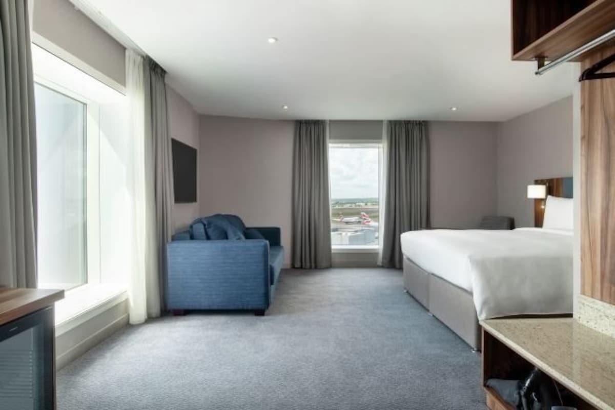 A hotel room with a large window, a bed, a blue sofa, and a desk.