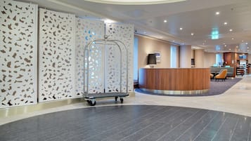 A modern hotel lobby with a reception desk, a service cart, and a decorative wall with geometric patterns.