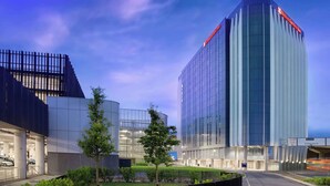 A modern hotel with a curved glass facade, a parking garage, and a well-maintained garden area.