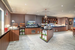 A modern kitchen area with a fruit display, a coffee station, and a seating area. - Hilton Garden Inn London Heathrow Terminal 2 and 3 (Hounslow)