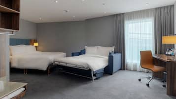 A hotel room with two beds, a desk, a chair, a lamp, and a large window with curtains.