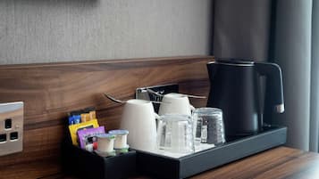 A hotel room's side table with a coffee maker, cups, and condiments.