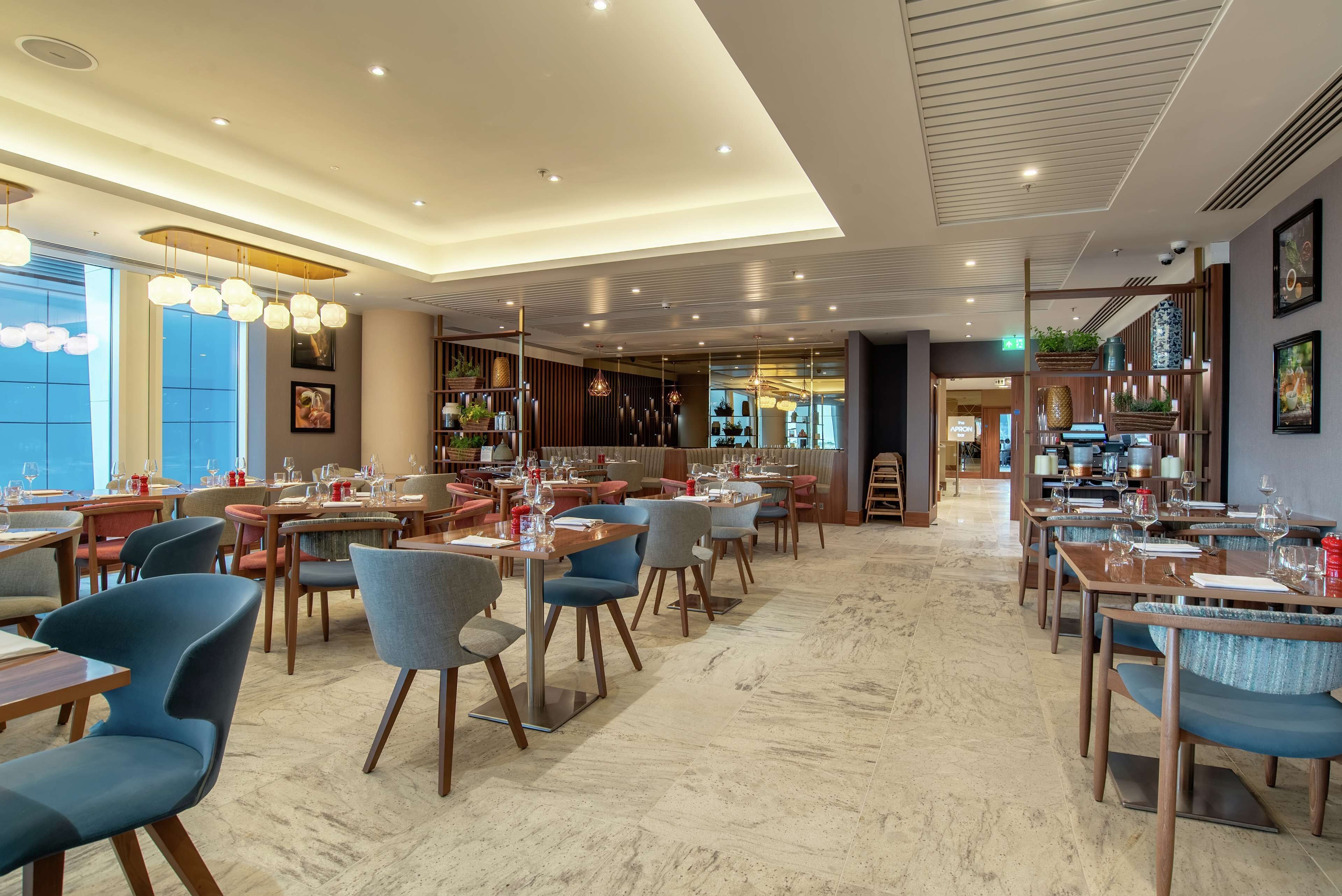 A spacious restaurant with multiple dining areas, modern lighting fixtures, and a view of the outdoors through large windows.