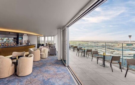 A modern lounge area with a bar, comfortable seating, and a view of an airport.